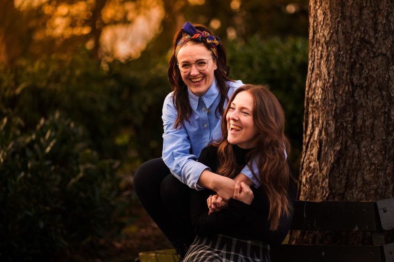 Engagement shoot same sex couple sat on bench laughing happy