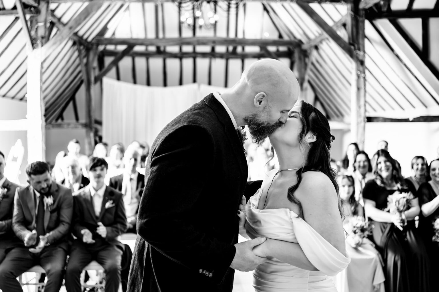 Bride and groom's first kiss in a barn ceremony, black and white