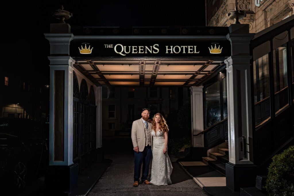 Bride and groom standing under the illuminated canopy sign at The Queens Hotel Southsea at night