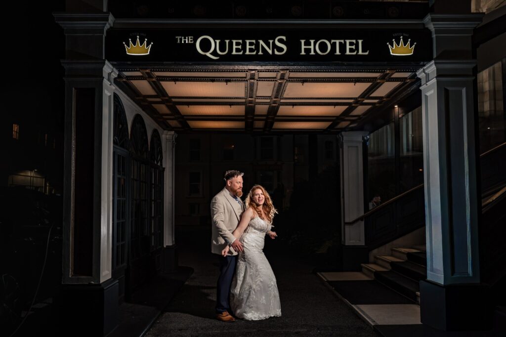 Bride laughing and dancing with the groom at the entrance of The Queens Hotel Southsea at night