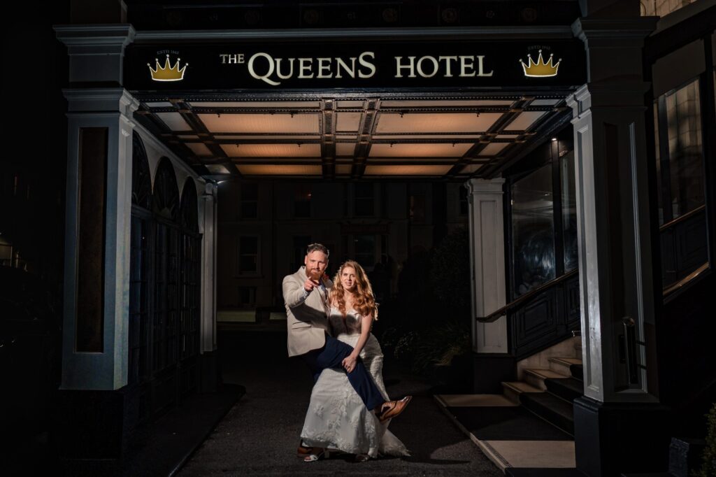 Groom pointing at the camera with his leg across the bride under the canopy at The Queens Hotel Southsea
