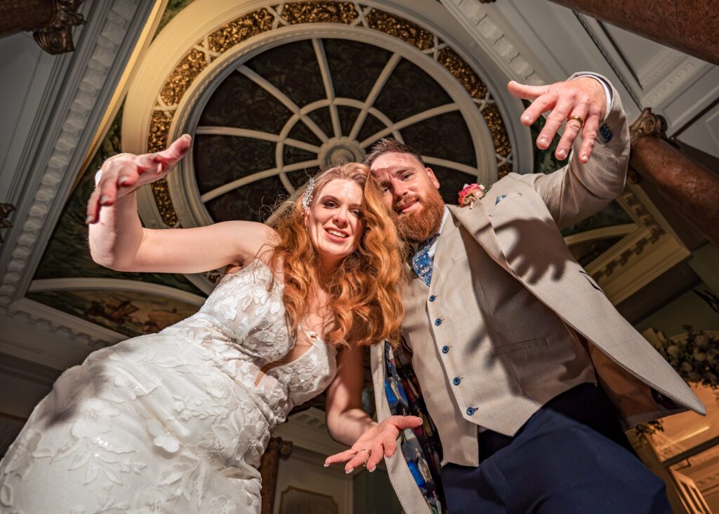 Low angle flash-lit portrait of bride and groom striking a pose beneath the painted dome at The Queens Hotel Southsea