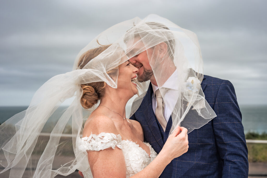 Bride and groom laughing under her veil in the sea breeze at Hotel Miramar Bournemouth