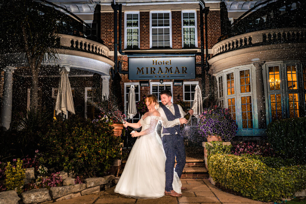 Bride and groom spraying champagne outside Hotel Miramar Bournemouth at night, lit with off camera flash