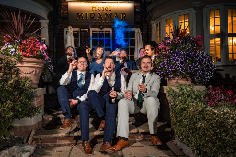 Groomsmen smoking cigars on the steps of Hotel Miramar at night, flash lit portrait