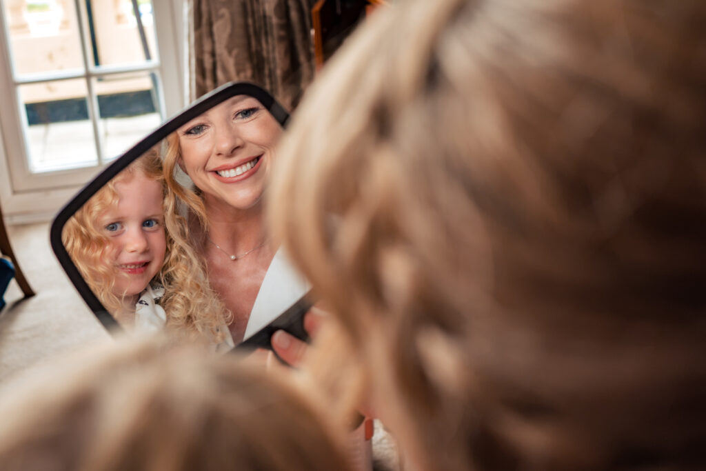 Bride smiling into a hand mirror during bridal prep at Hotel Miramar Bournemouth