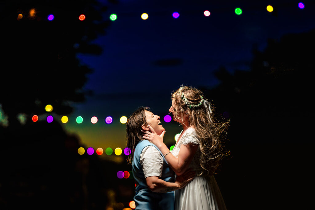 Two brides embracing under festoon lights in the evening near Southsea Castle