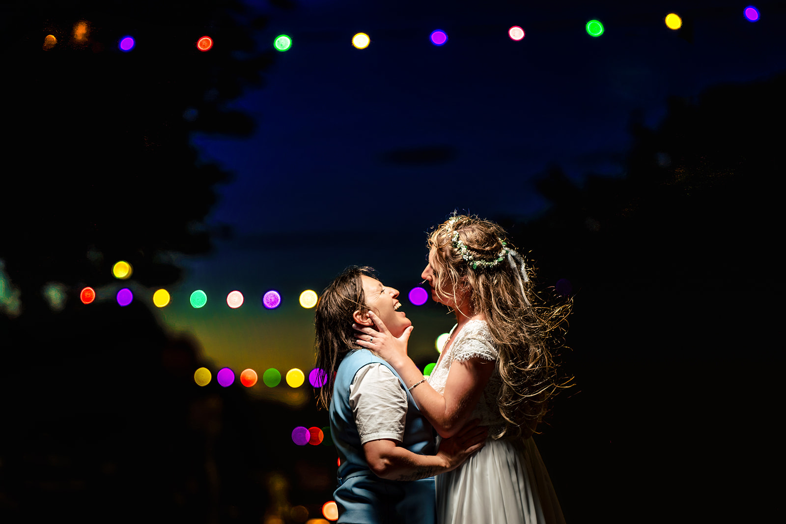 Two brides embracing under festoon lights in the evening near Southsea Castle