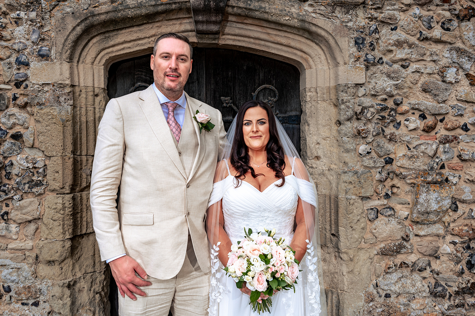 Bride and groom stood in the doorway of St Thomas à Becket Church, Warblington, looking to camera