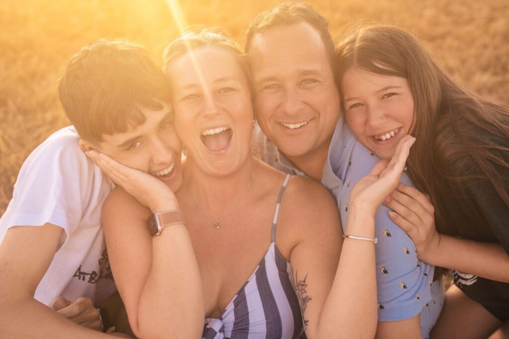 Emma Staley laughing with her husband and two children in a golden field at sunset