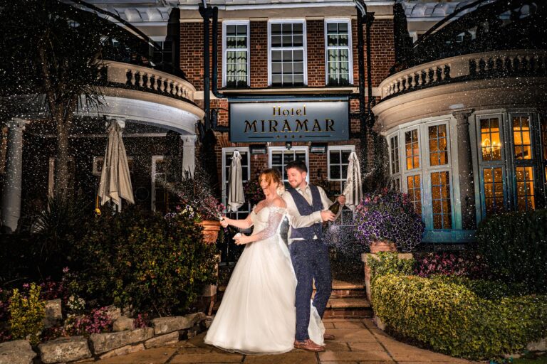 Bride and groom spraying champagne outside Hotel Miramar Bournemouth at night, lit with off camera flash
