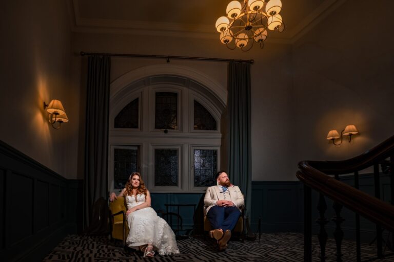 Bride and groom sitting in yellow armchairs on the staircase landing at The Queens Hotel Southsea, lit with off camera flash