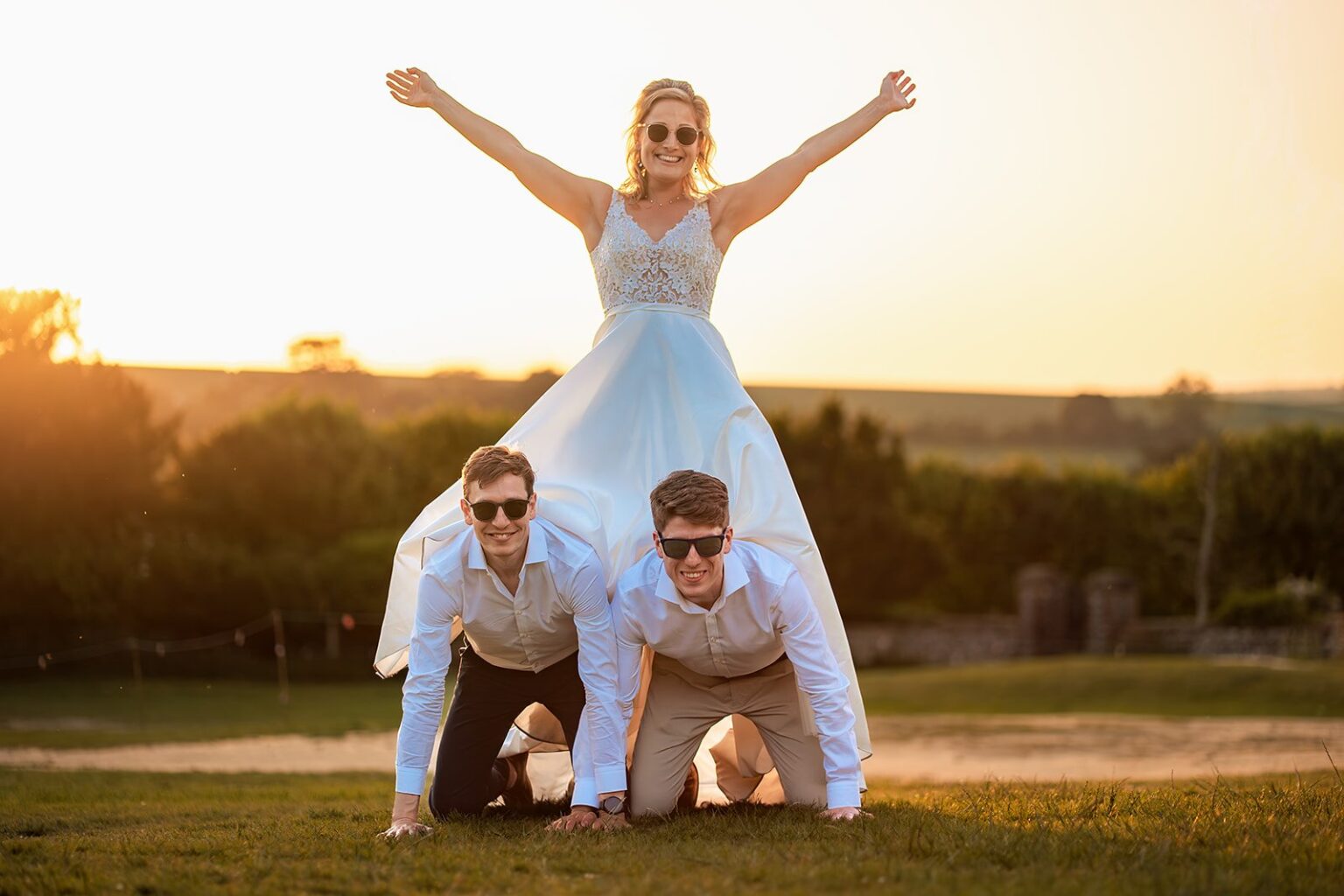 Bride standing on the groomsmen's backs in a human pyramid at sunset at Great Ballard School