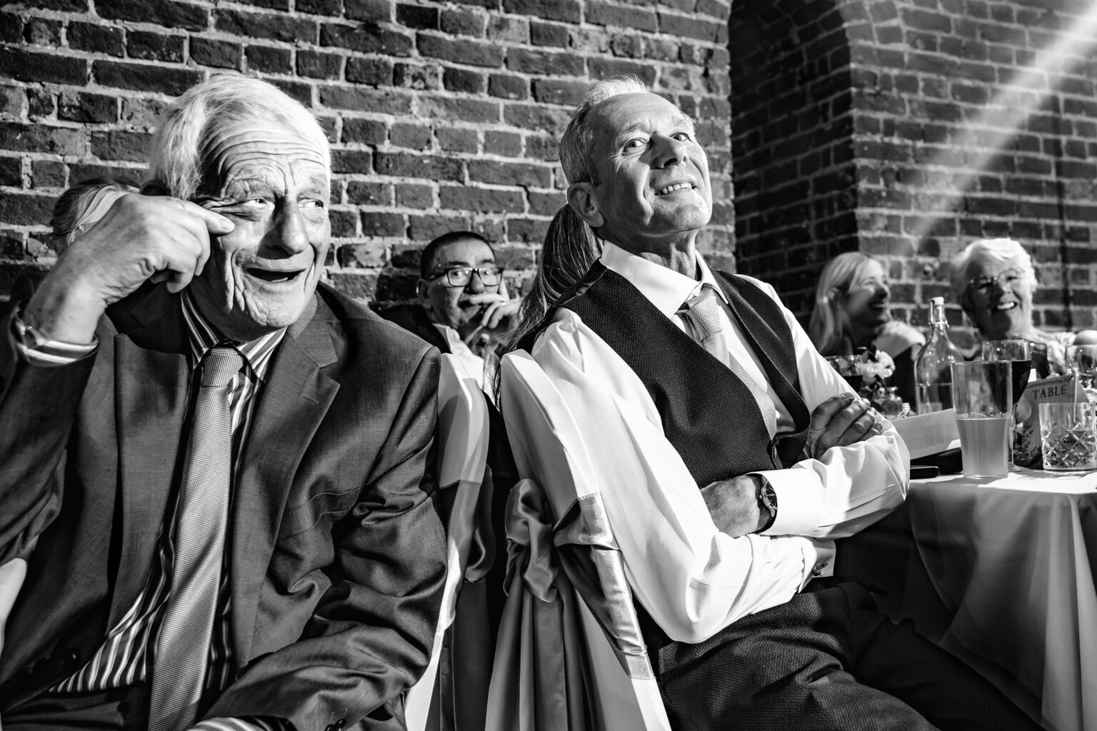 Two guests laughing during the wedding speeches, black and white