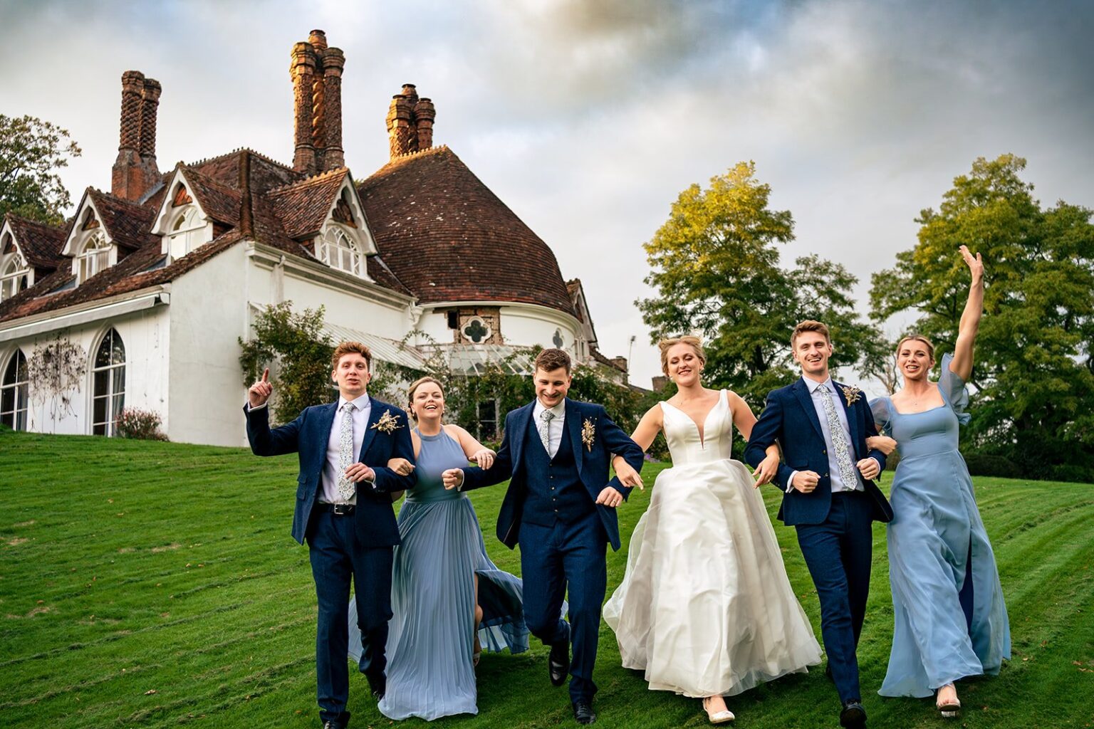 Bride, groom and wedding party running across the lawn at Houghton Lodge Gardens