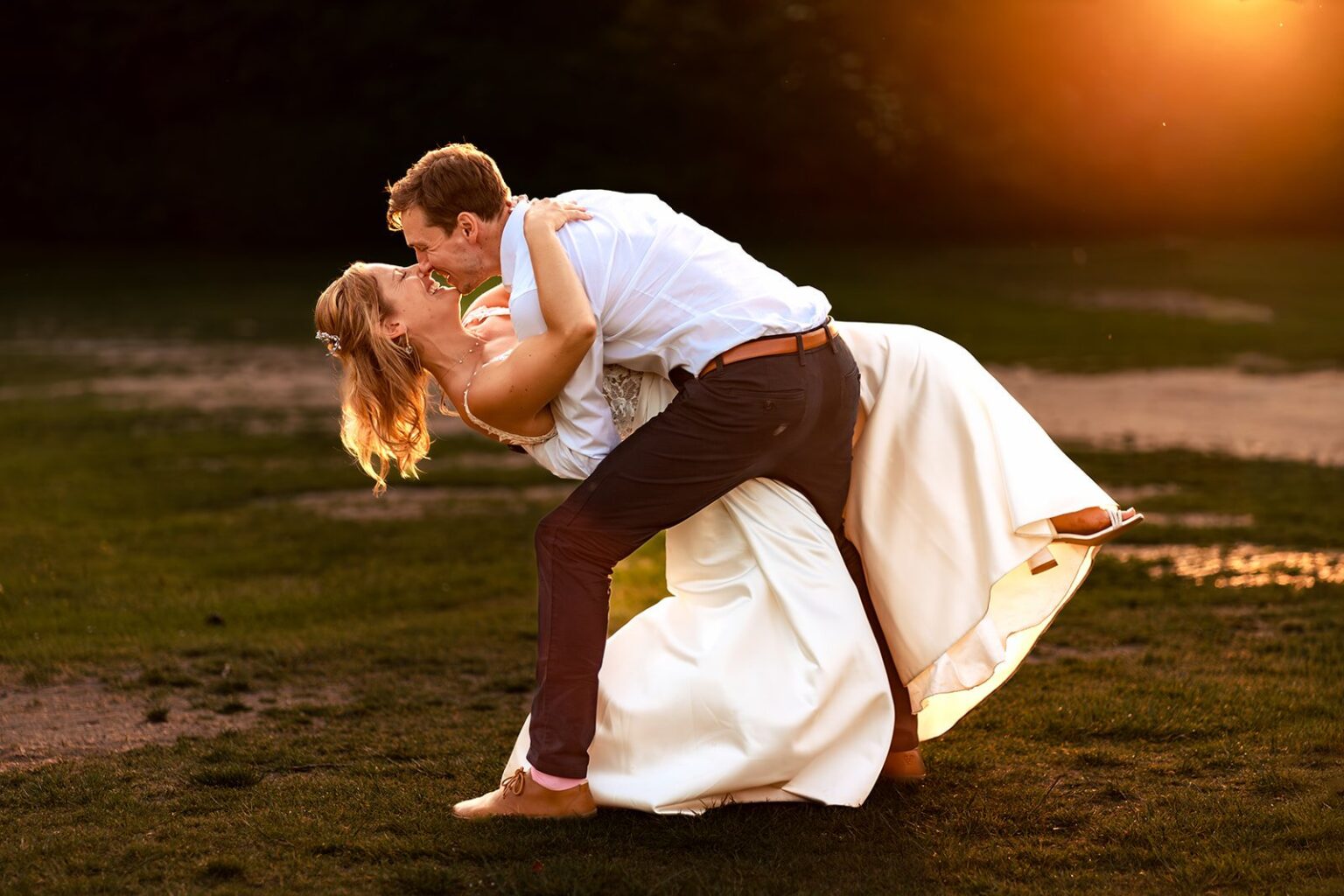 Groom dipping the bride for a kiss at sunset at Great Ballard School