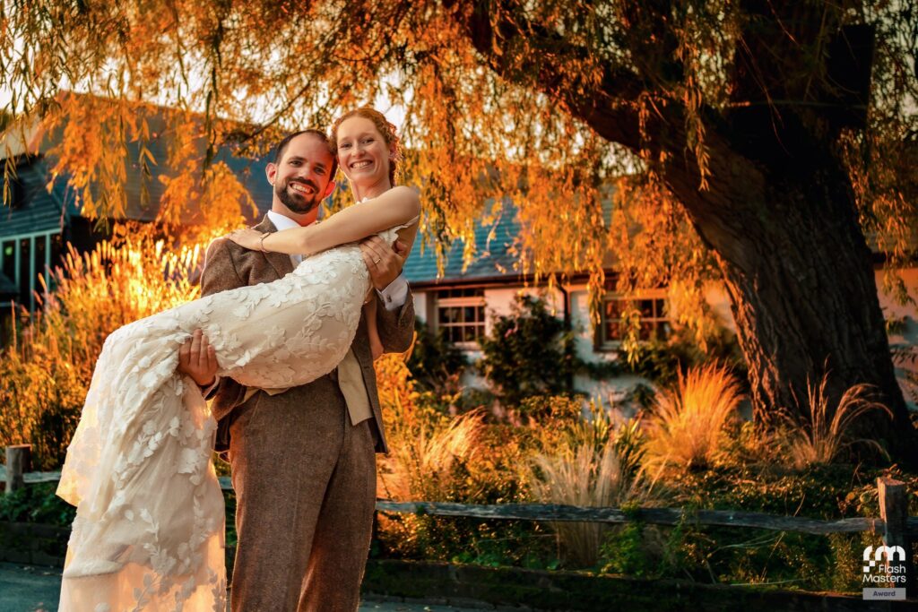 Groom carrying the bride under a golden willow tree, lit with off camera flash