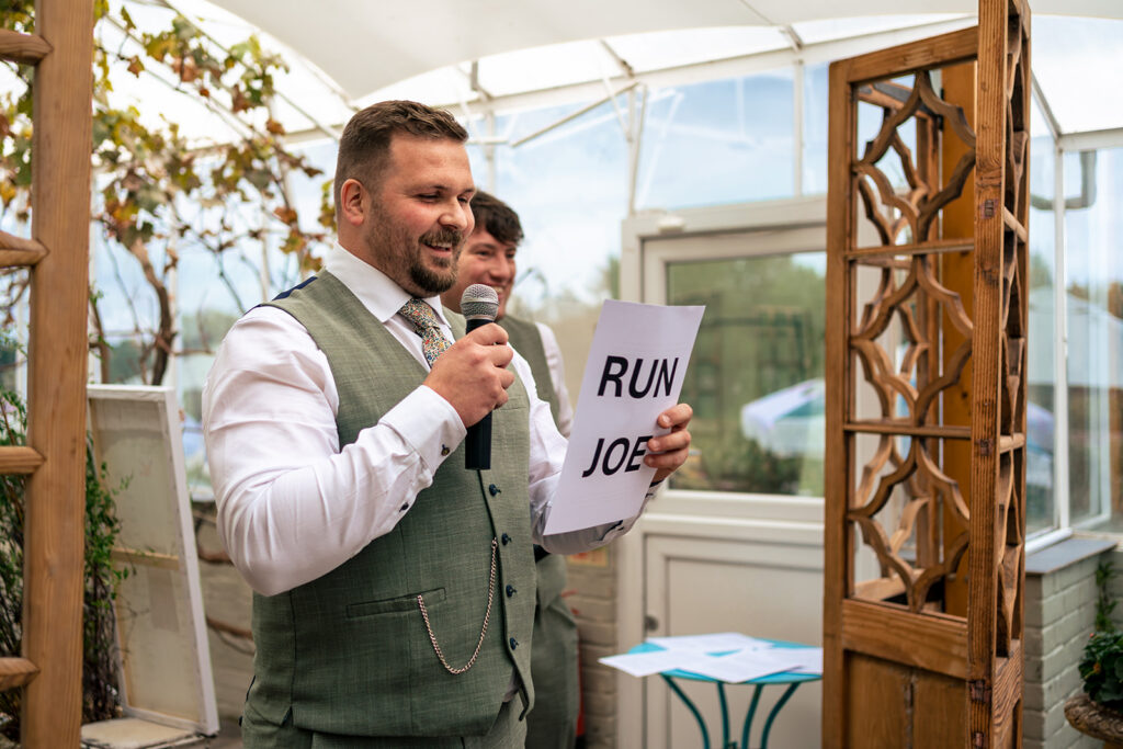 Best man holding up a RUN JOE sign during his speech at Houghton Lodge Gardens