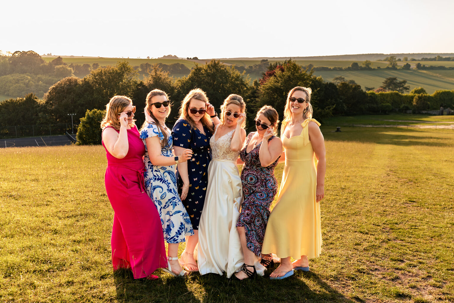 Bride and bridesmaids in sunglasses striking a pose at sunset at Great Ballard School