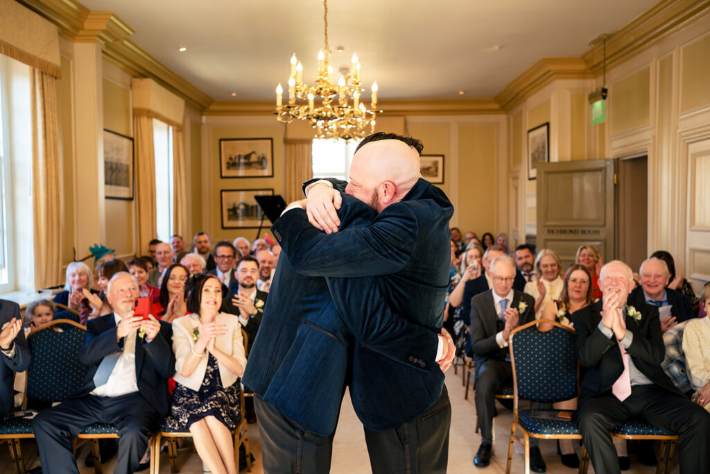 Grooms kissing as guests cheer at Edes House, Chichester, West Sussex
