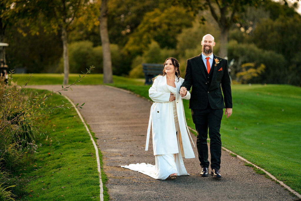 Bride and groom walking hand in hand on an autumn path at Skylark Golf and Country Club, Whiteley