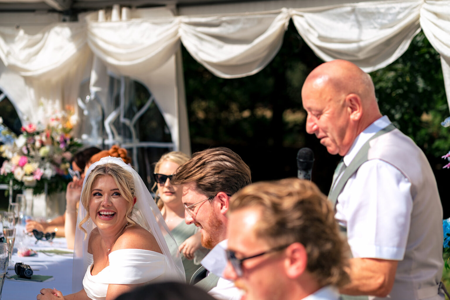 Bride beaming as a guest gives his speech