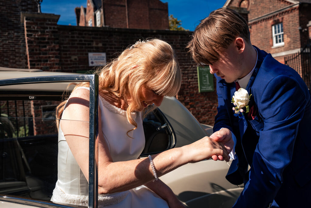 Bride's son helping her out of the vintage wedding car at Portsmouth Register Office, Hampshire