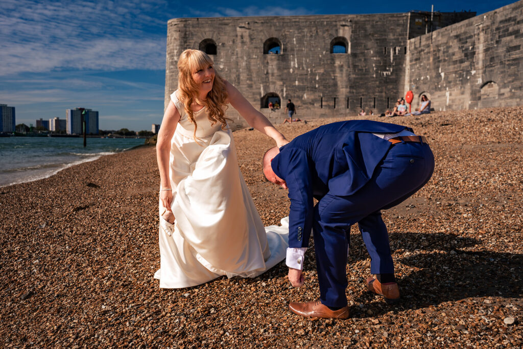 Groom taking the bride's shoes off on the beach at the Hot Walls, Old Portsmouth