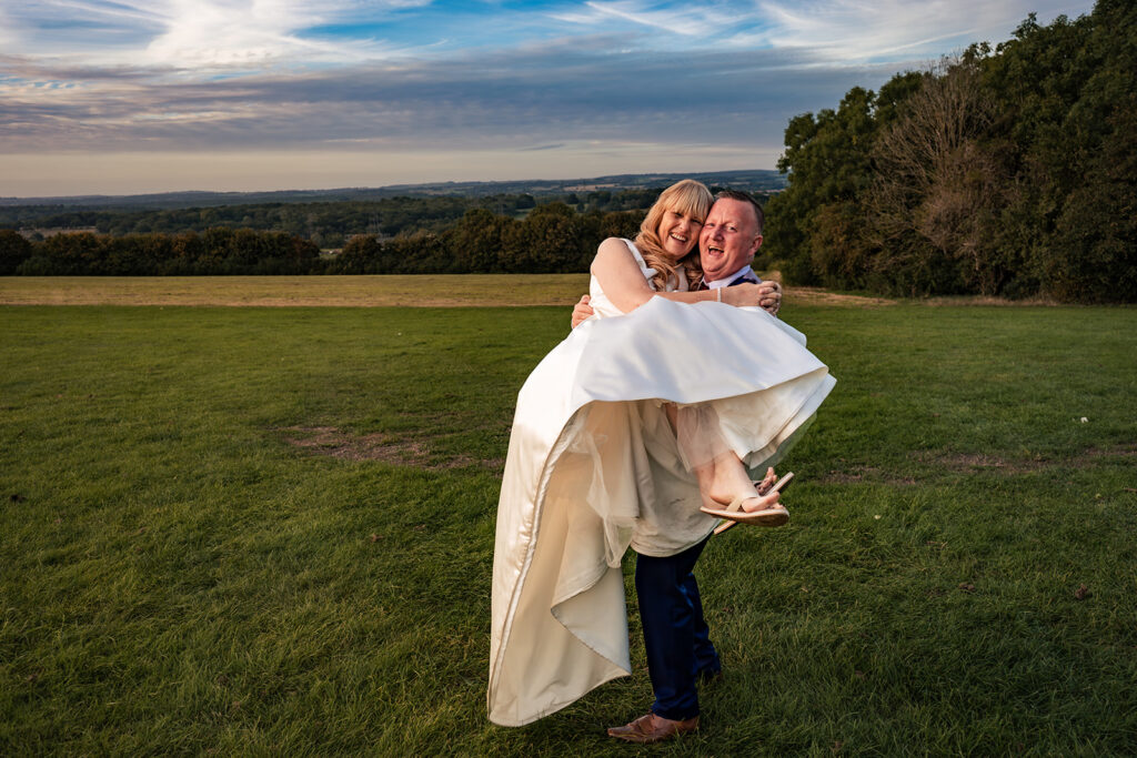 Groom carrying the bride in a field overlooking the South Downs at sunset, next to The Churchillian, Portsdown Hill