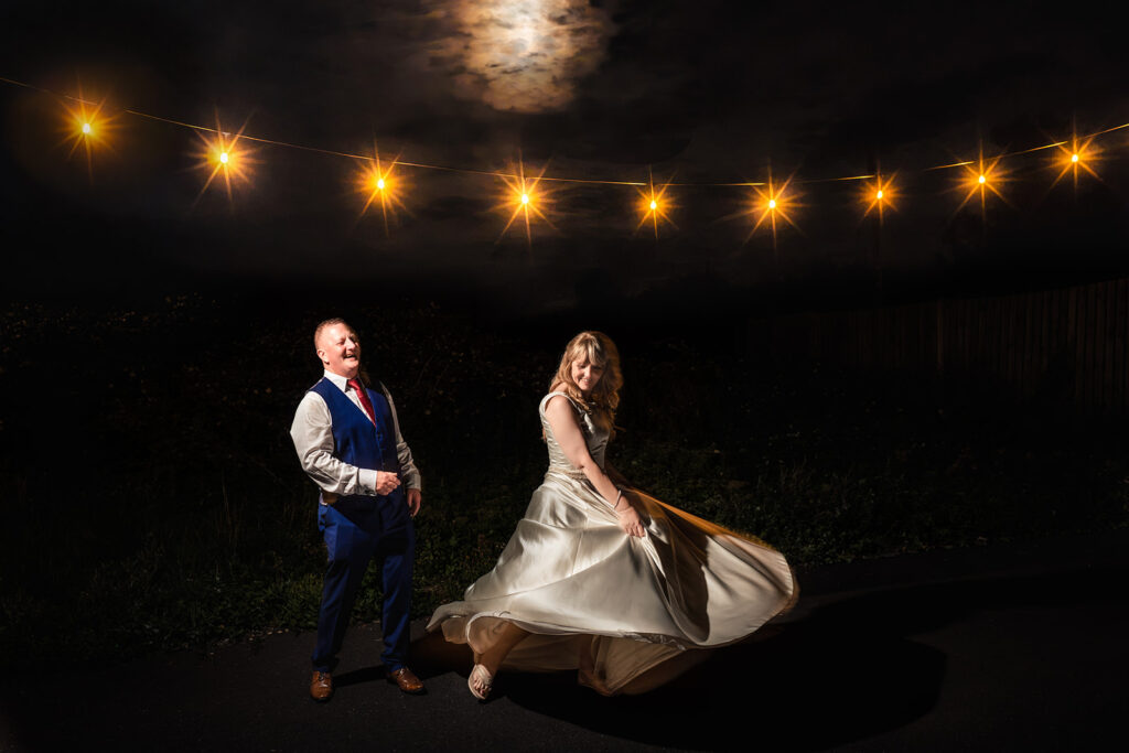 Bride twirling under festoon lights with the groom at night, lit with flash, at The Churchillian, Portsdown Hill, Portsmouth