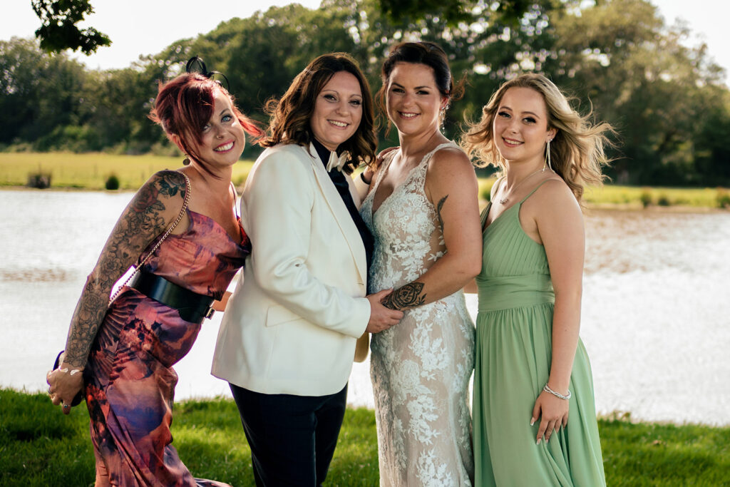 Two brides with their bridesmaids by the lake at Southlands Barn, West Sussex