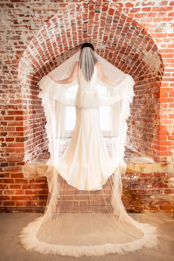 Wedding dress hanging in a brick window at Southsea Castle, Portsmouth (styled shoot)