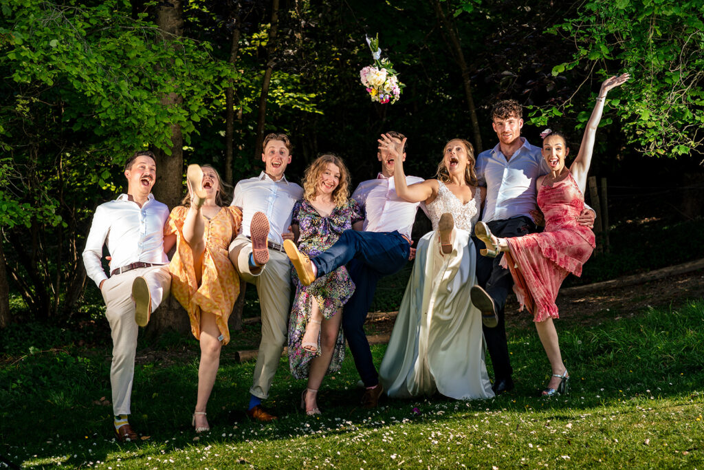 Bridal party jumping on the lawn at Great Ballard School, Eartham