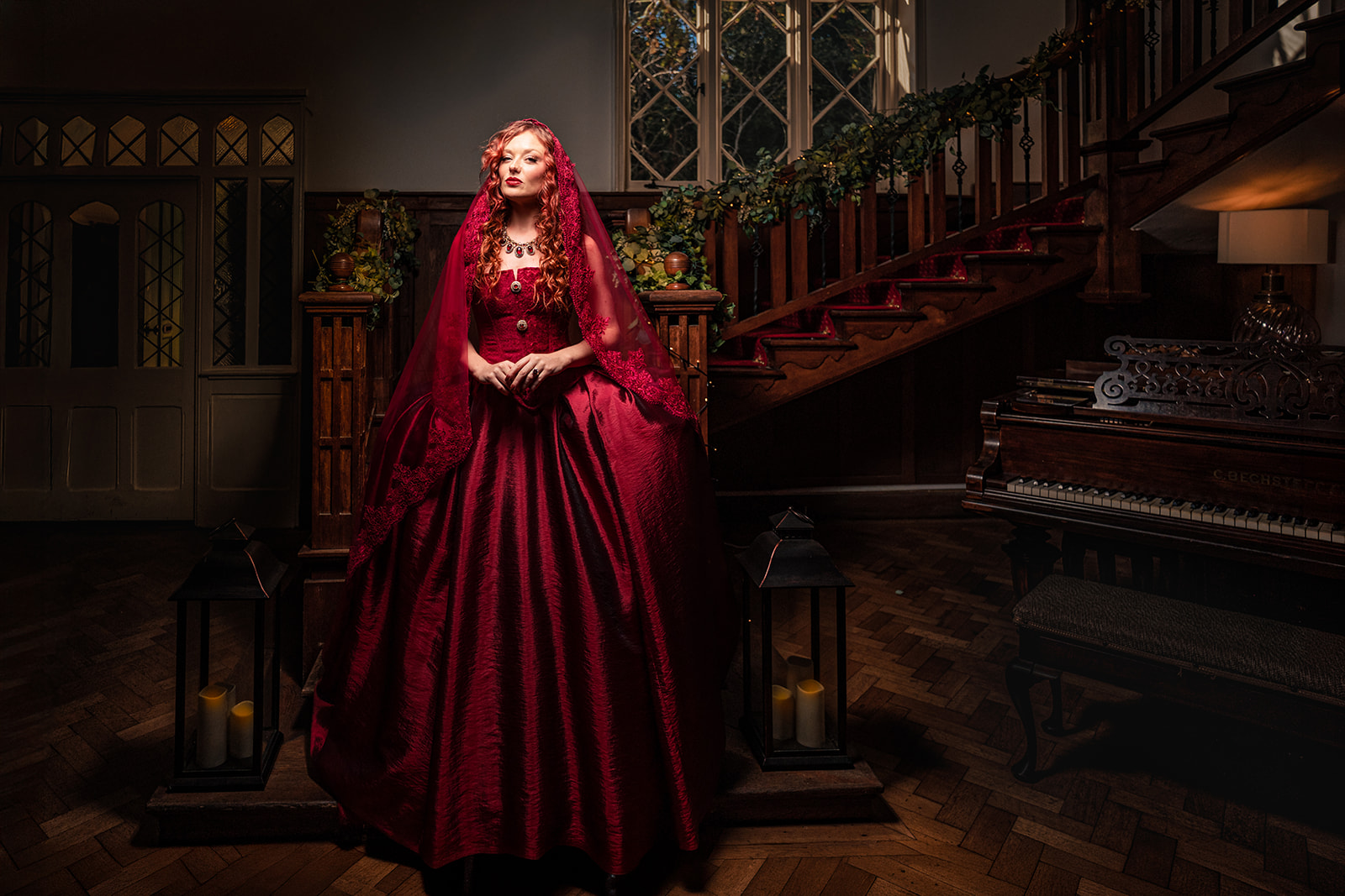 Bride in a red gown and lace veil in the grand hallway at The Alverbank, Gosport, framed by lanterns and the staircase