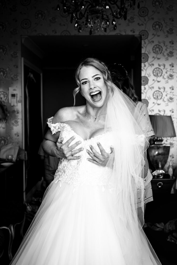 Bride laughing as her dress is fastened during bridal prep at Hotel Miramar Bournemouth, black and white