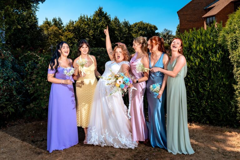 Bride and bridesmaids in rainbow dresses cheering at Newtown House Hotel