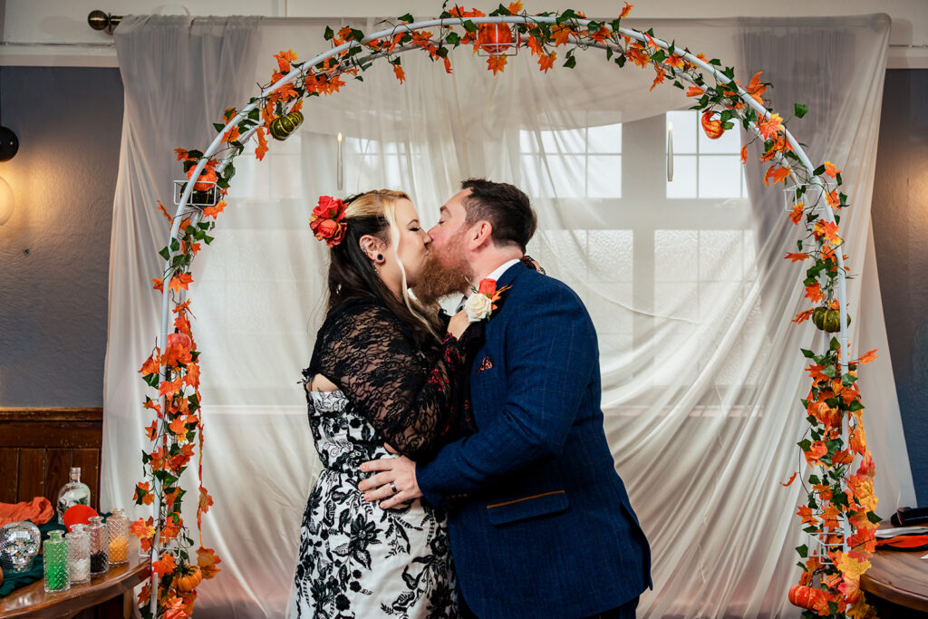 Just married kiss under the floral arch at Halloween micro wedding, Southampton