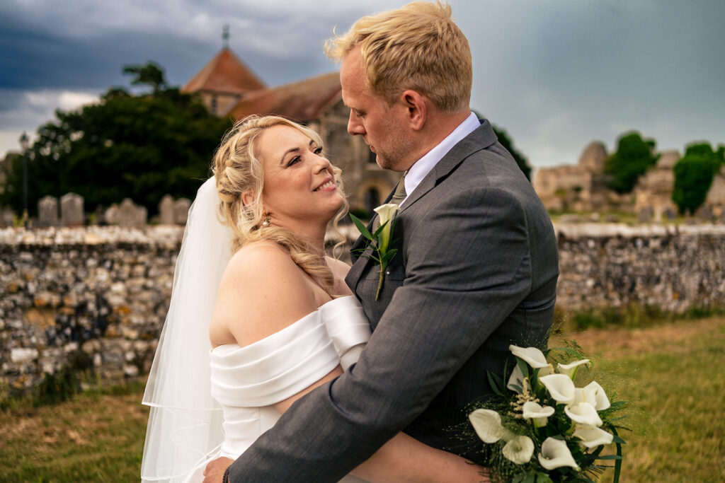 Groom kissing the bride by the castle walls at St Mary’s Church, Portchester