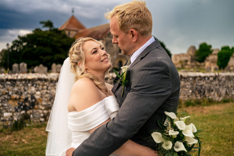 Groom kissing the bride by the castle walls at St Mary’s Church, Portchester