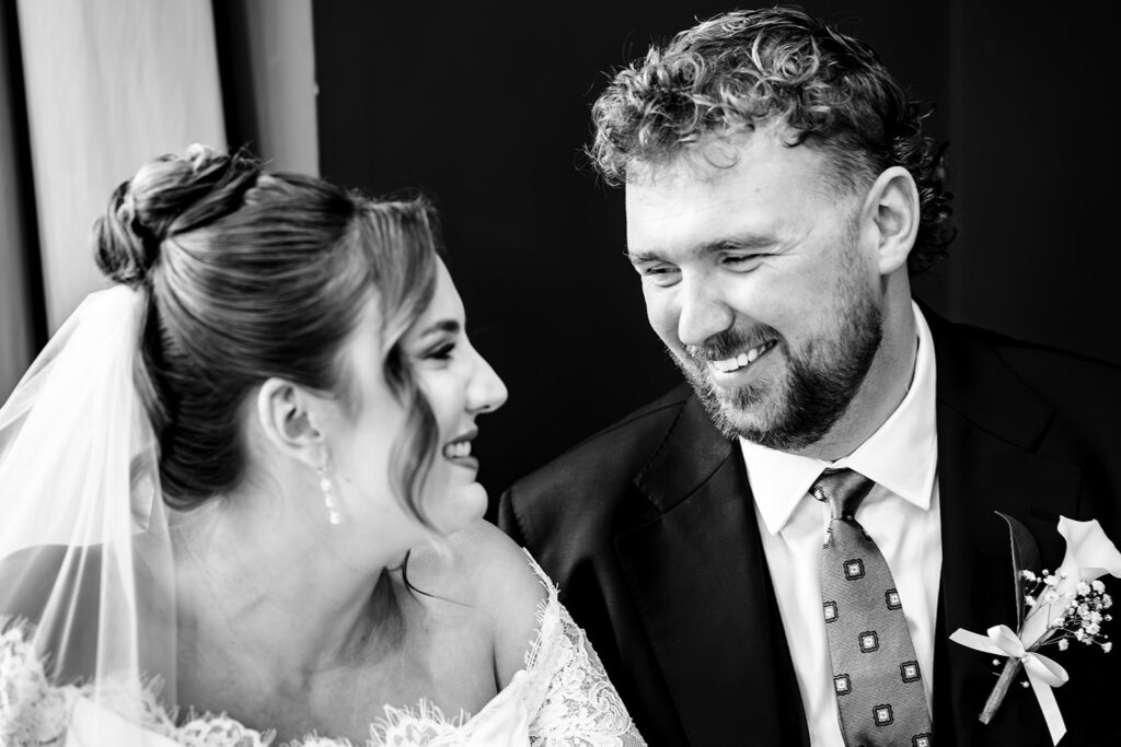 Bride and groom grinning at each other, black and white at Winchester Register Office