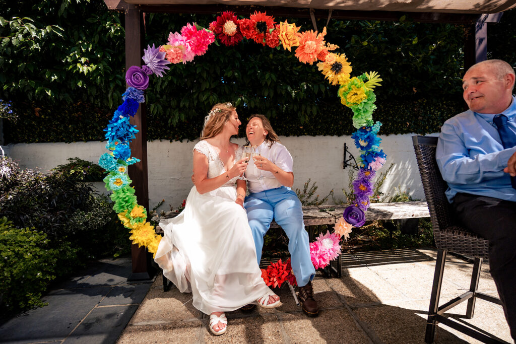 Two brides under a rainbow flower arch