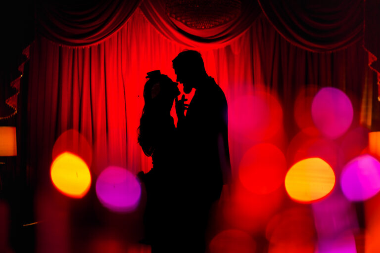 Silhouette of a couple kissing in front of red curtains with colourful bokeh, created with off camera flash