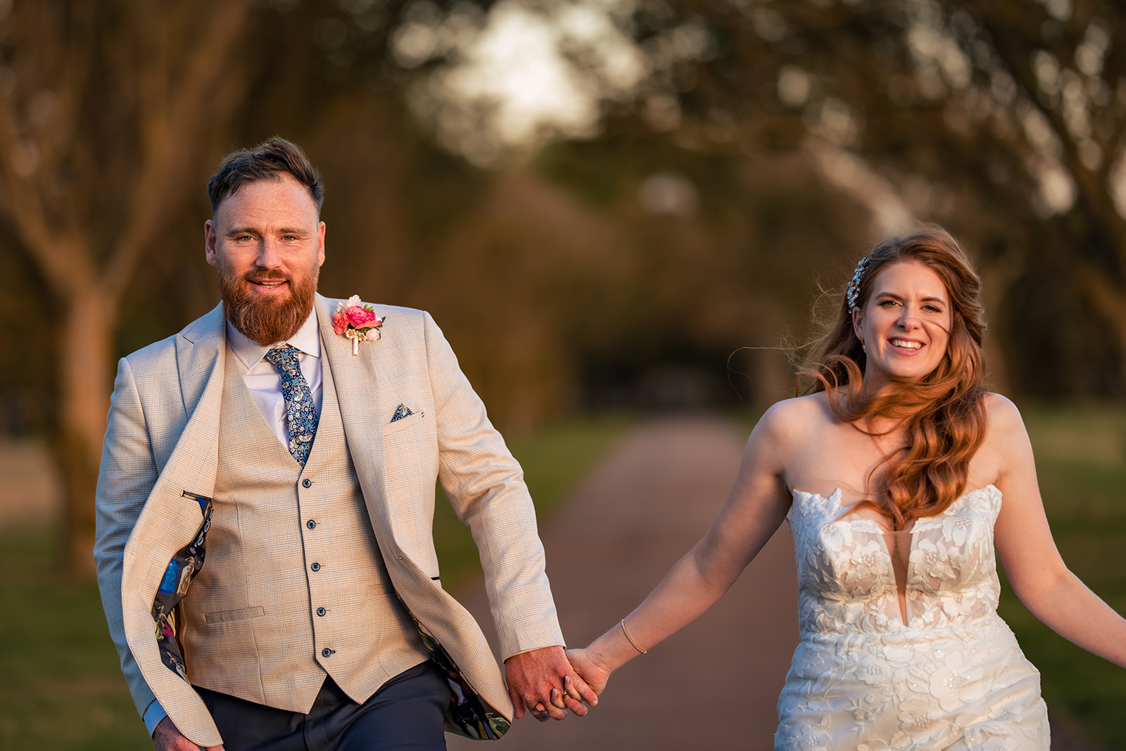 Bride and groom running hand in hand down a tree lined path on Southsea Common