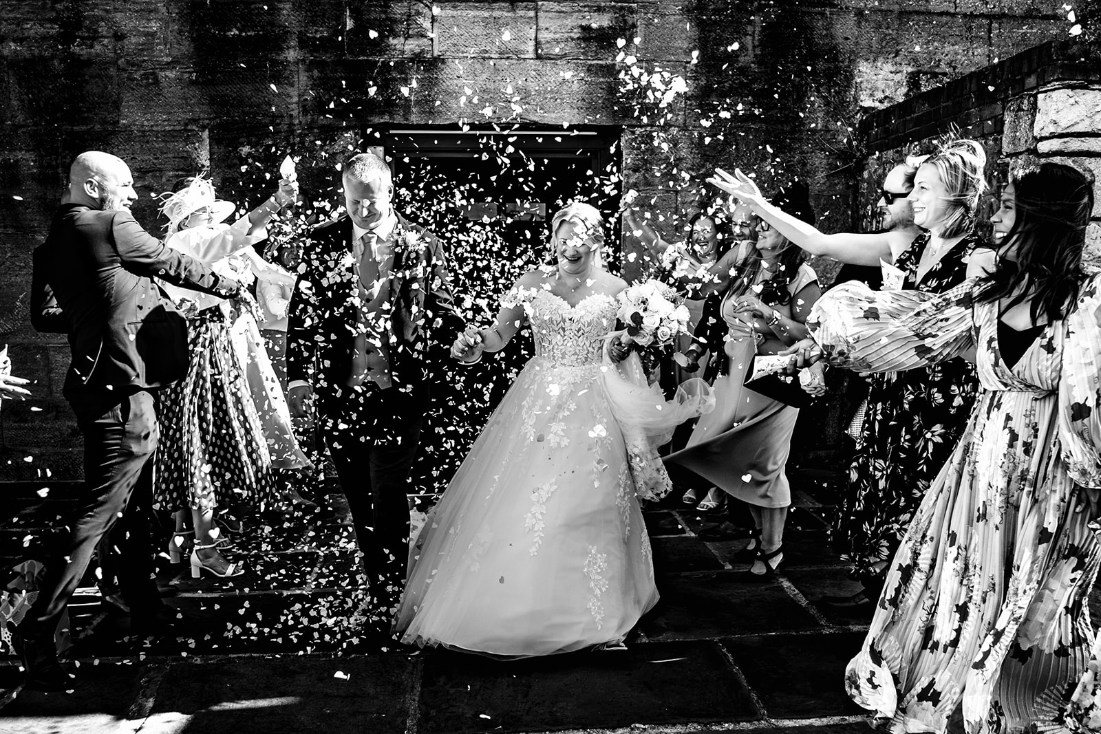 Confetti flying as the bride and groom leave The Square Tower, black and white