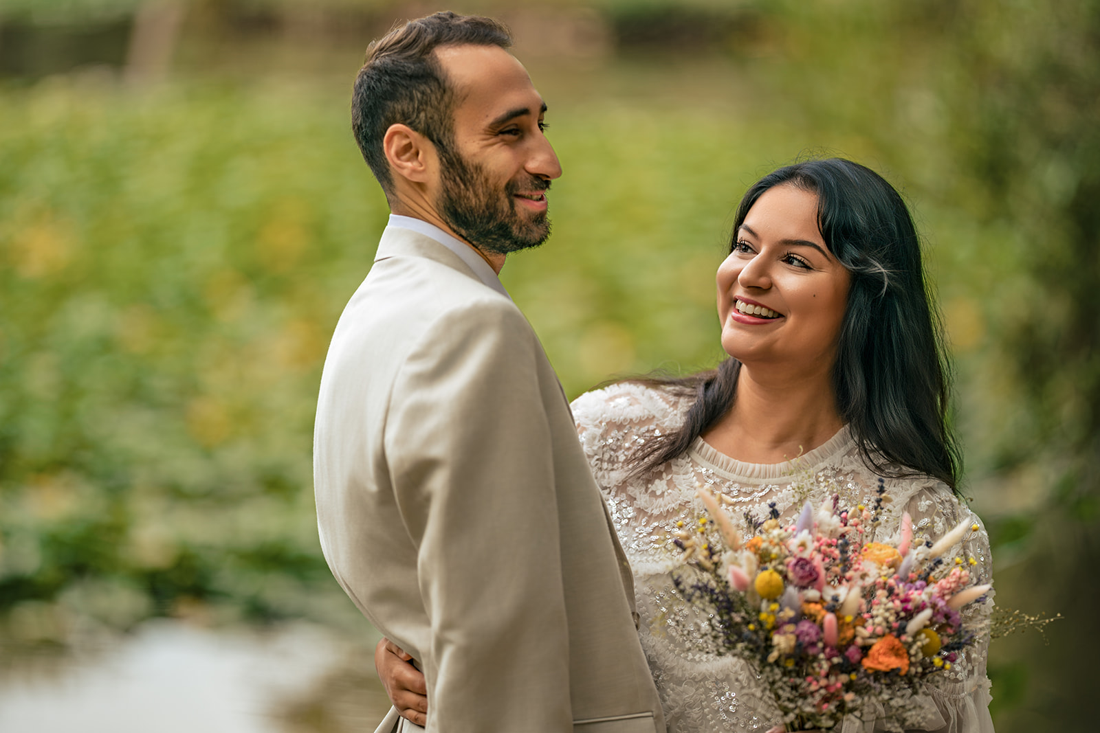 Bride and groom laughing at each other by the lake at Staunton Country Park