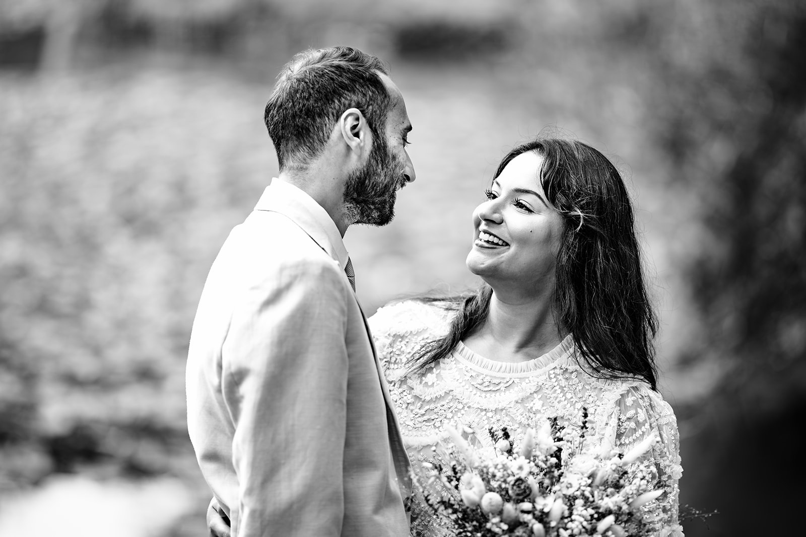 Bride smiling up at her husband by the lake at Staunton Country Park, black and white