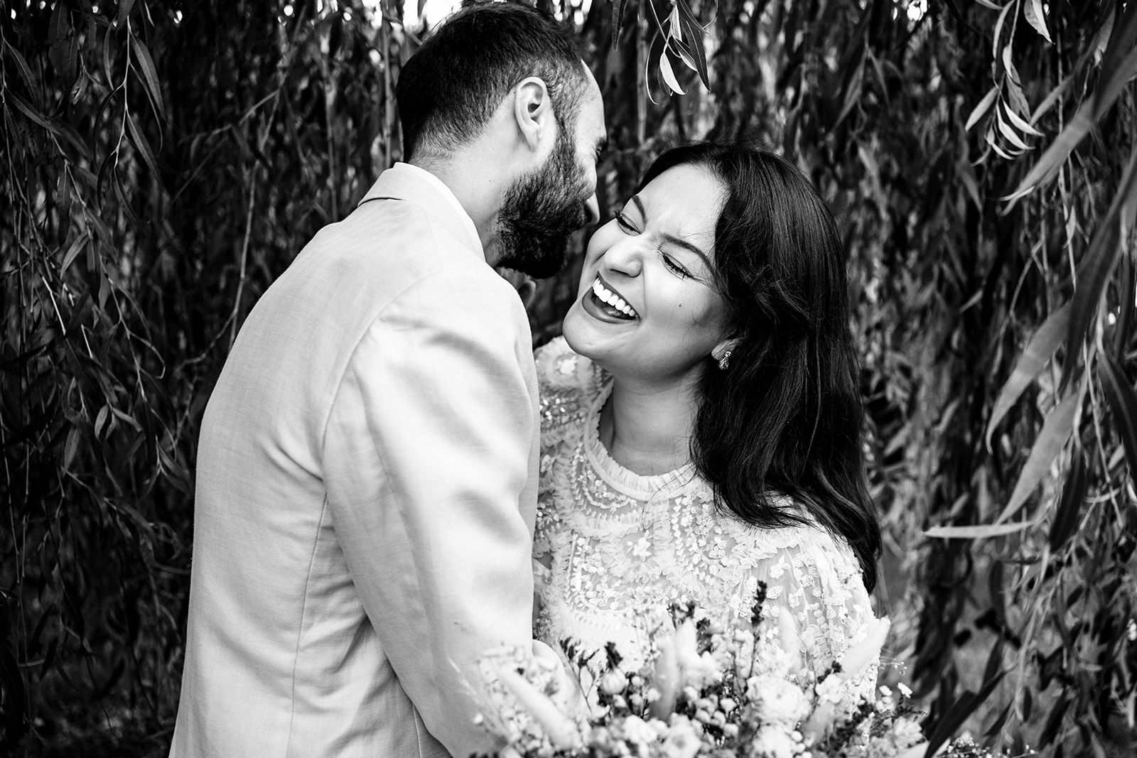 Bride laughing with her husband under the willows at Staunton Country Park, black and white