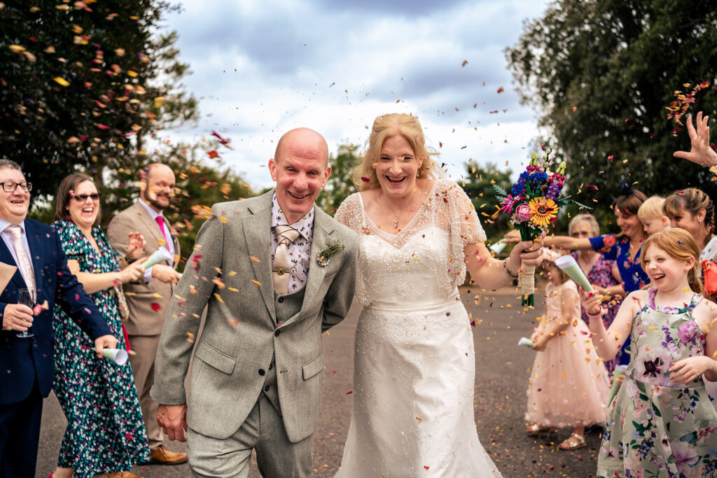 Bride and groom walking through a confetti tunnel at Lodge Hill Centre, West Sussex