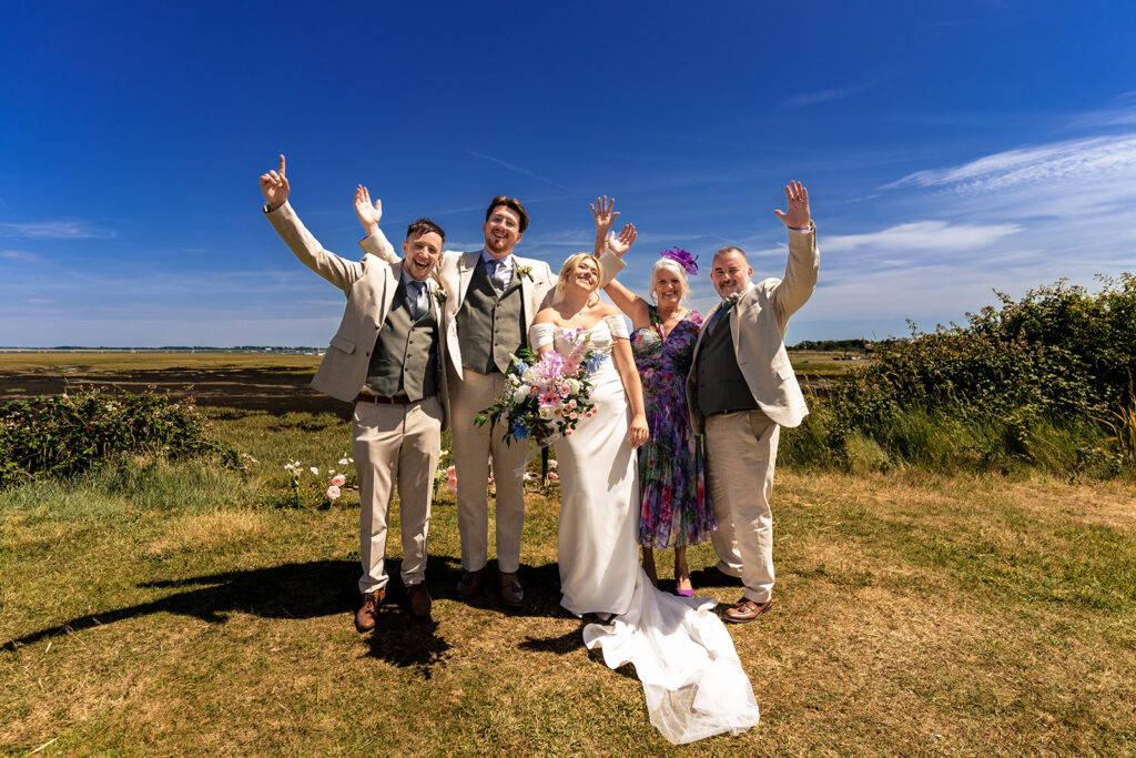 Groomsmen jumping for joy under a blue sky at Tournerbury Woods Estate, Hayling Island